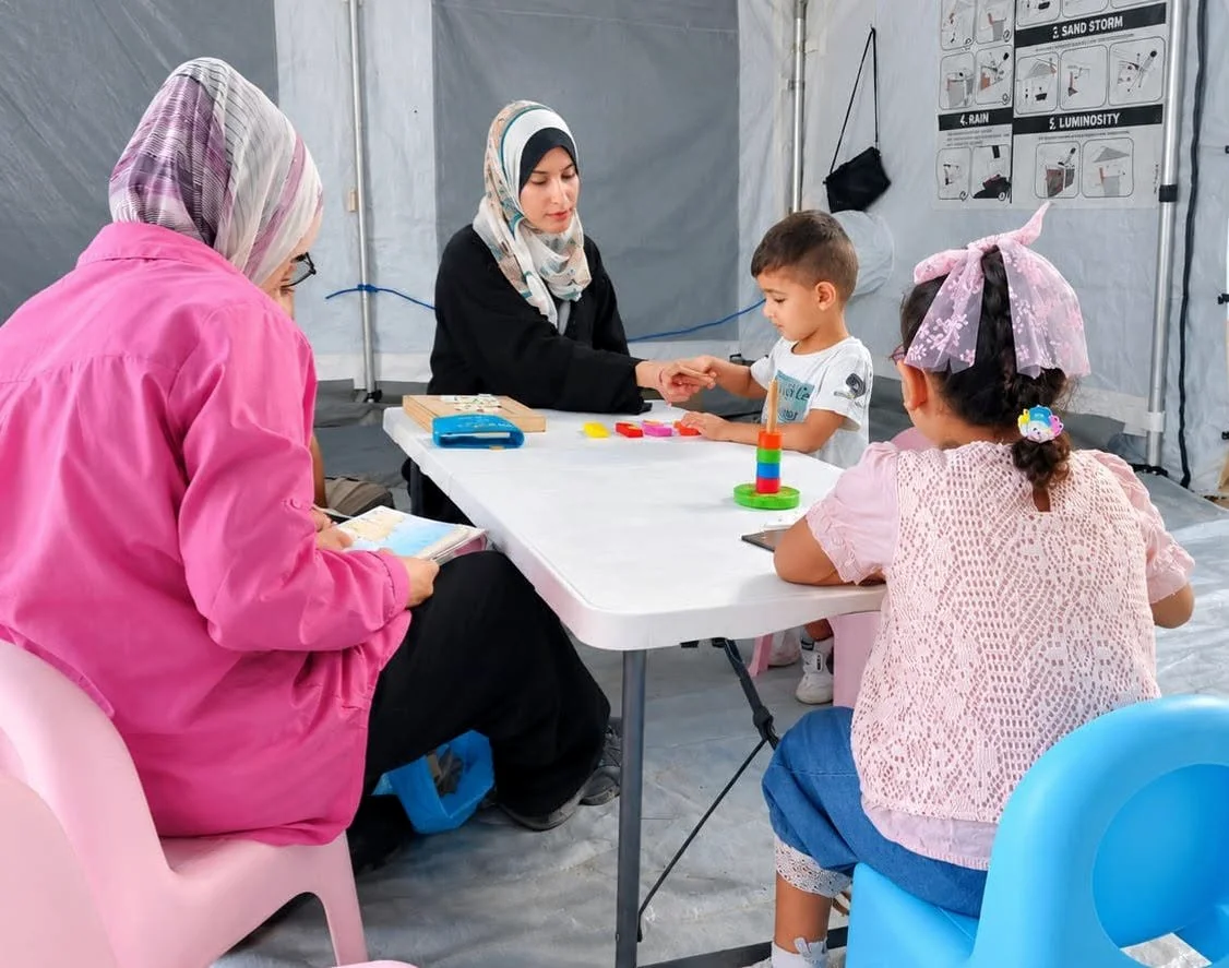 لقطة جماعية تضم أطفالًا وبالغين حول طاولة عليها مواد تعليمية