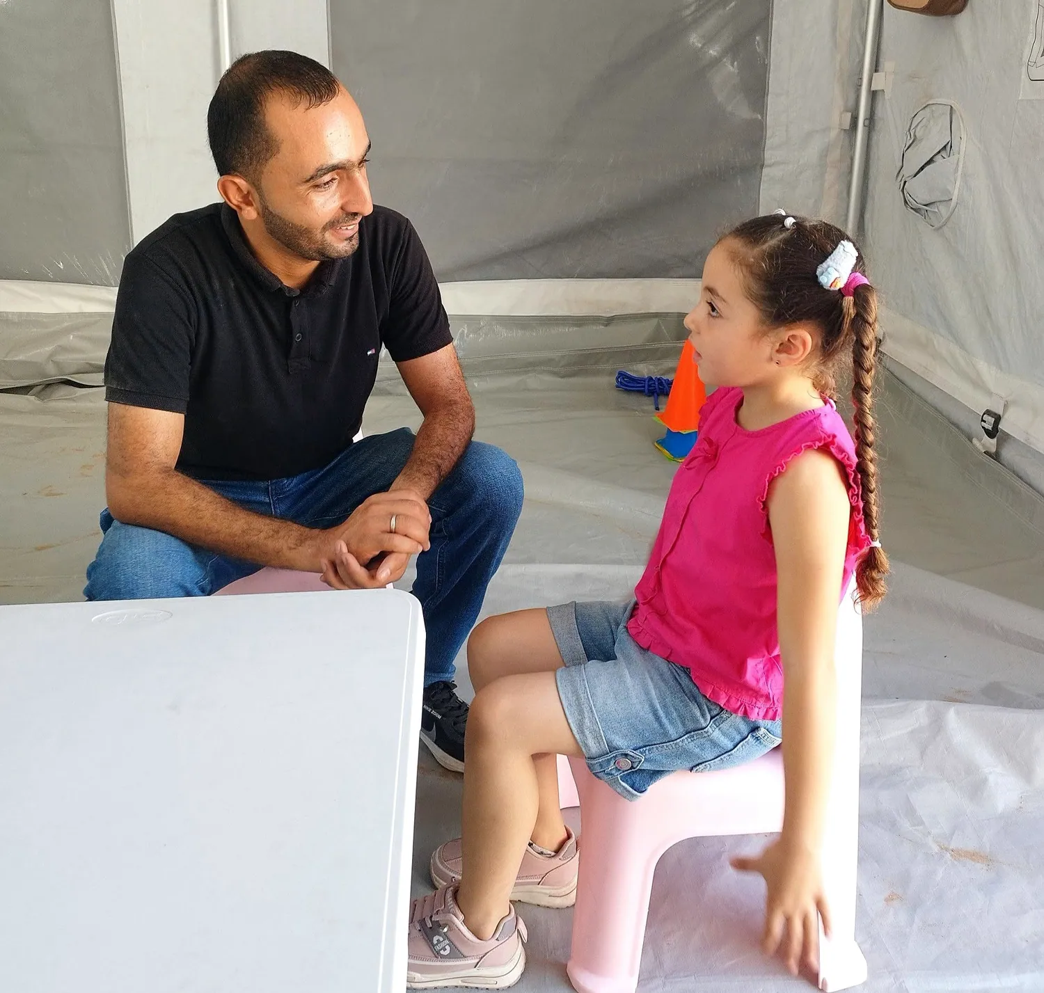 رجل يجلس ويتحدث مع طفلة ترتدي قميصًا ورديًا