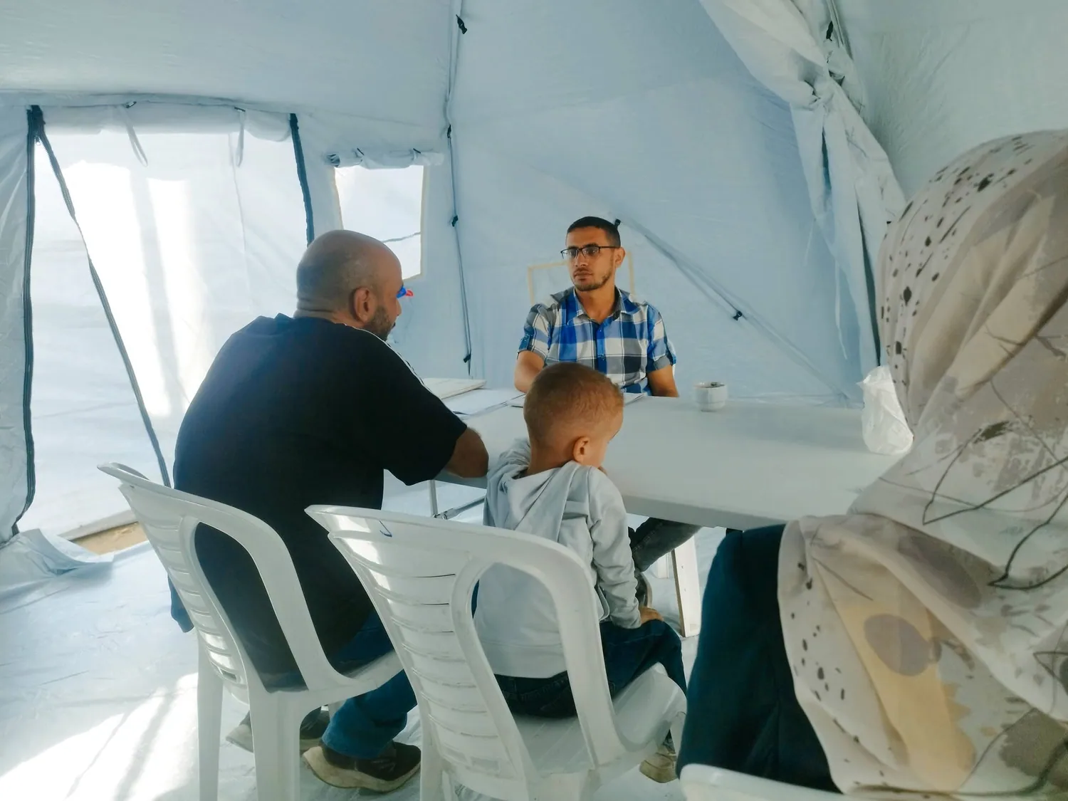 عدة أشخاص بينهم طفل يجلسون حول طاولة داخل خيمة