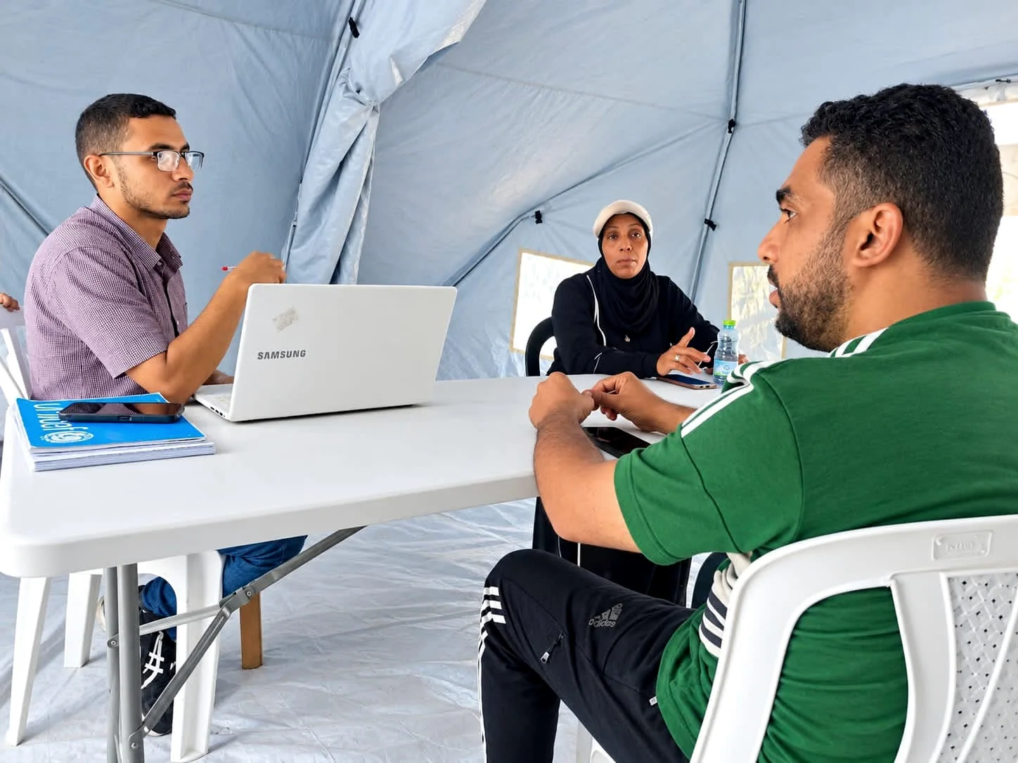 ثلاثة بالغين يجلسون حول طاولة للحوار داخل مساحة عمل مغطاة